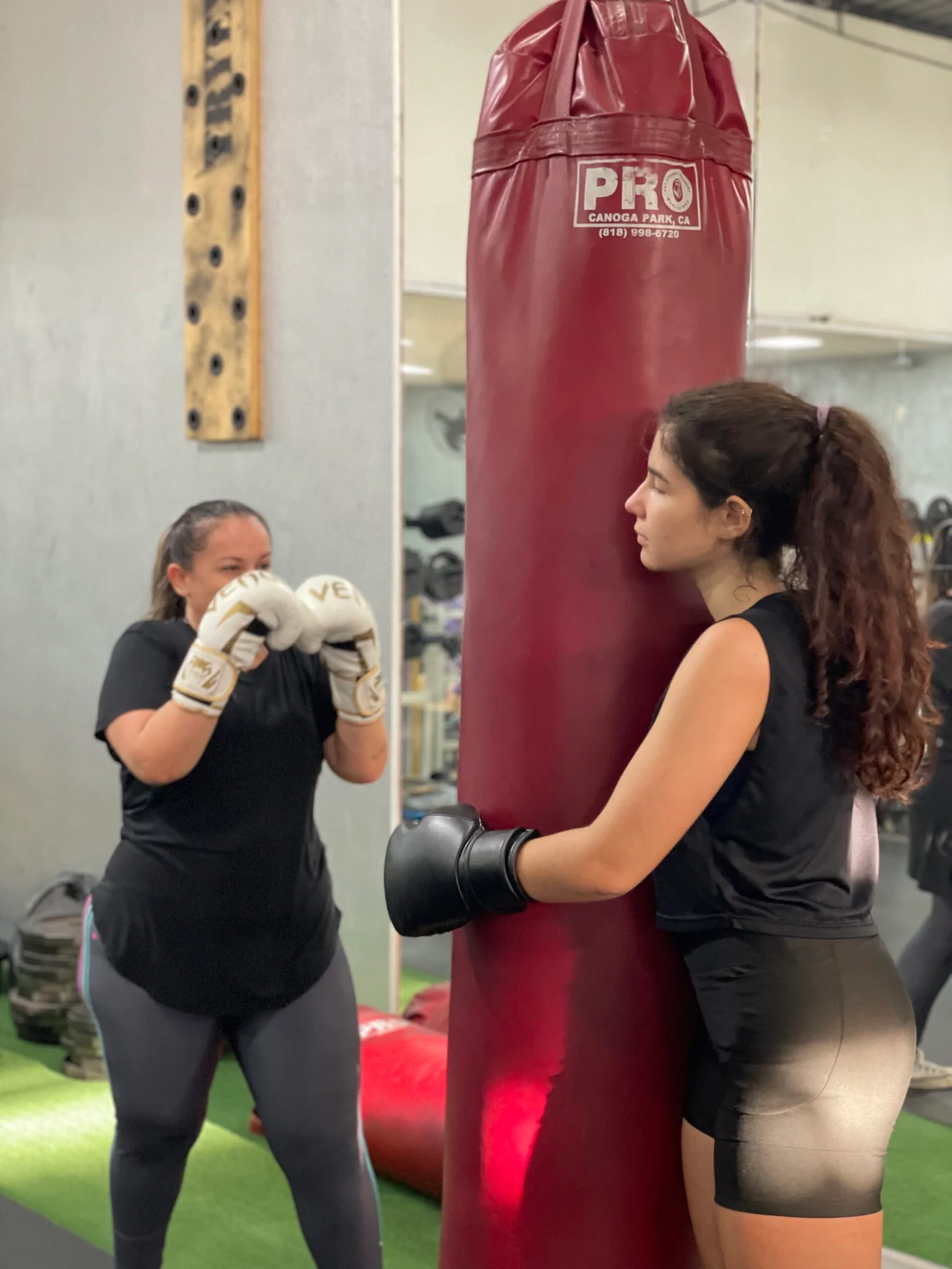 Duas alunas com luvas de boxe junto a um saco de pancada na MaxFit.