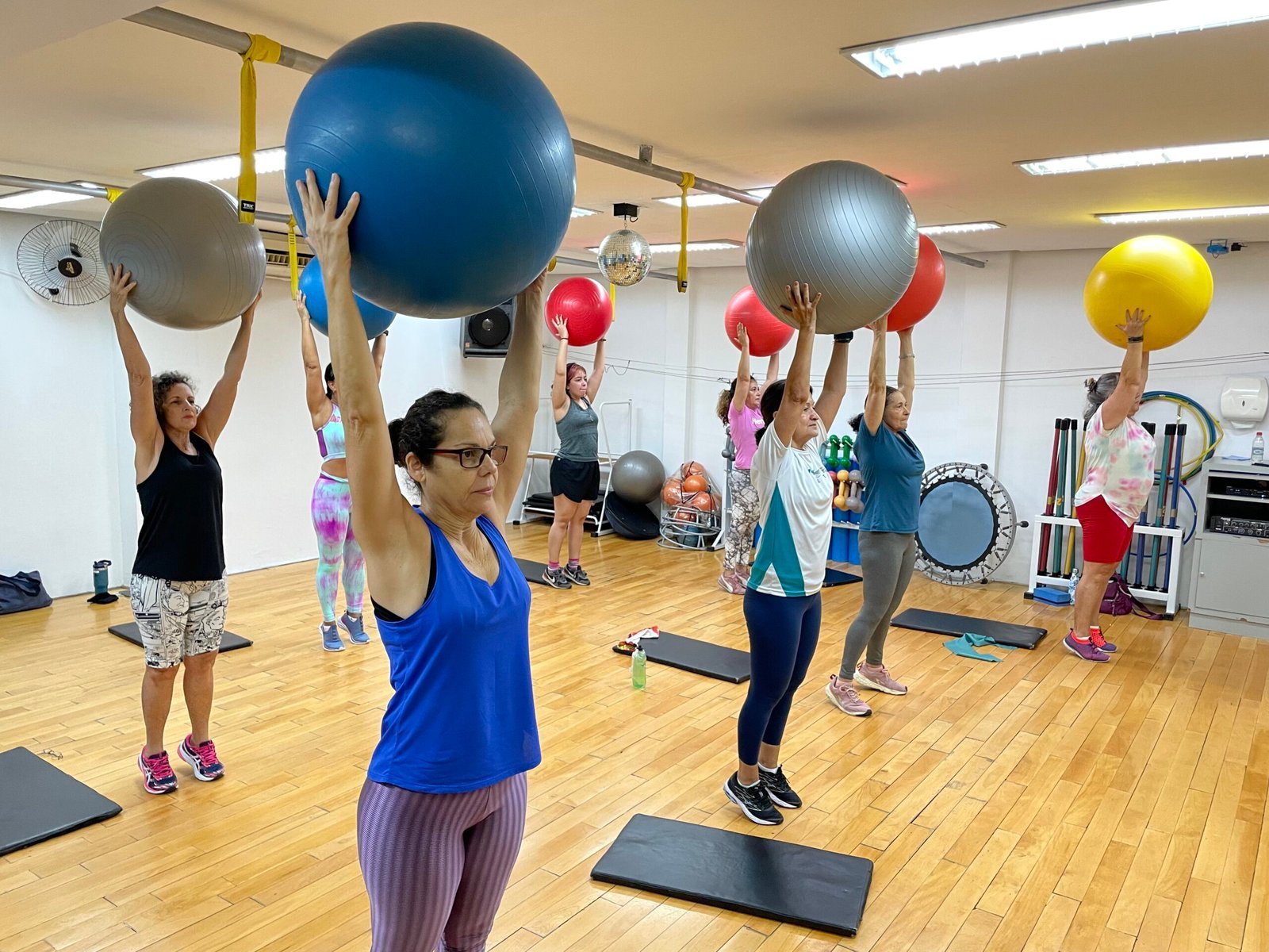 Alunas da MaxFit fazendo exercícios juntas, com bolas elevadas durante uma aula coletiva.