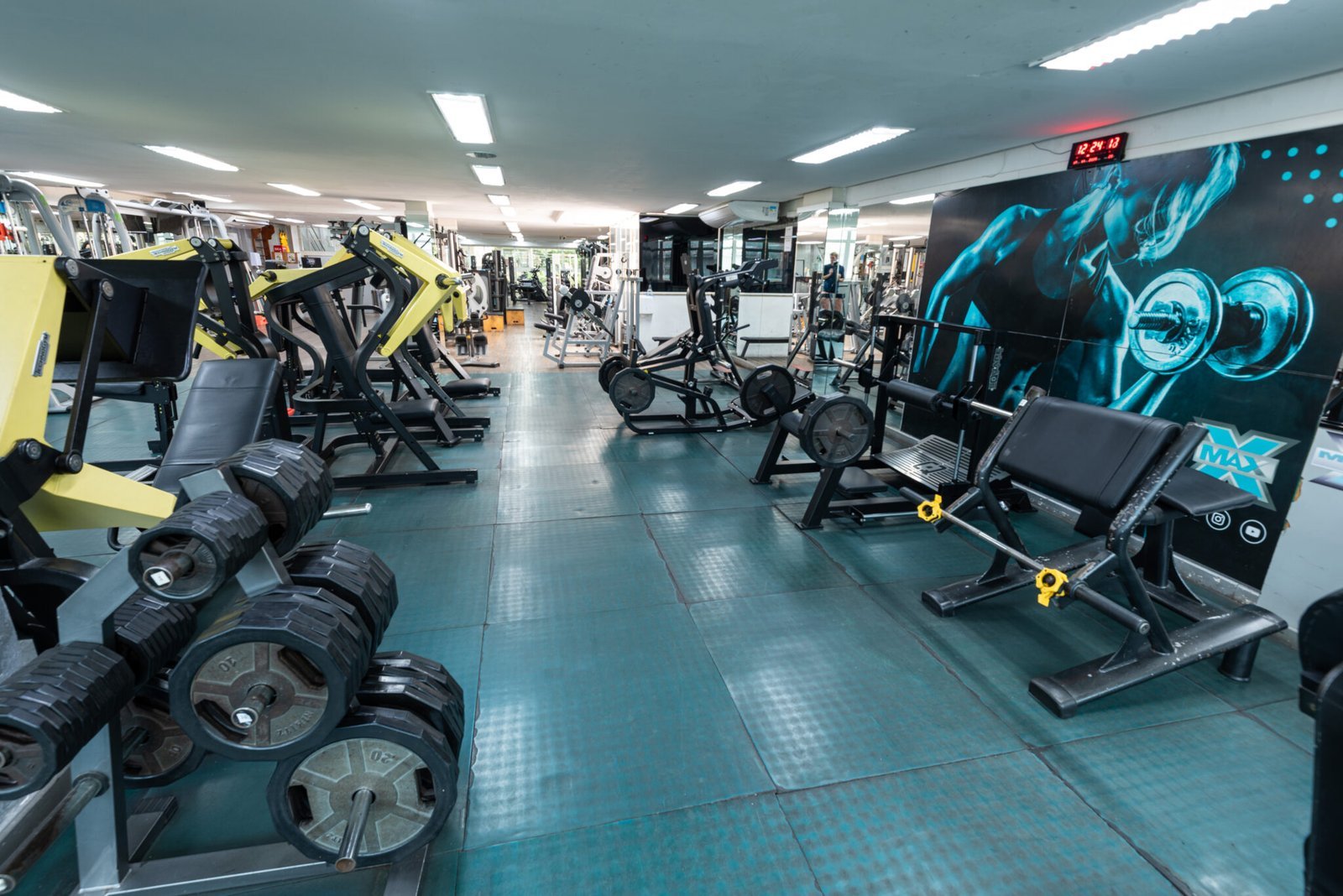 Salão de musculação da MaxFit, com halteres, aparelhos e o mural Tiffany da academia.